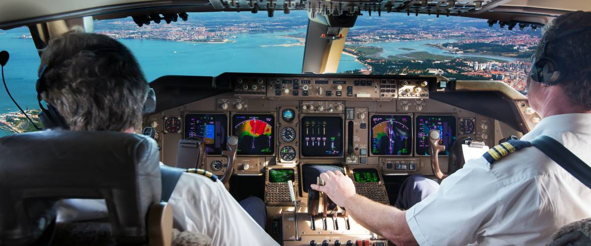 The cockpit of modern jet airplane. Aircraft flies above the city landscape and river. Pilots at work.