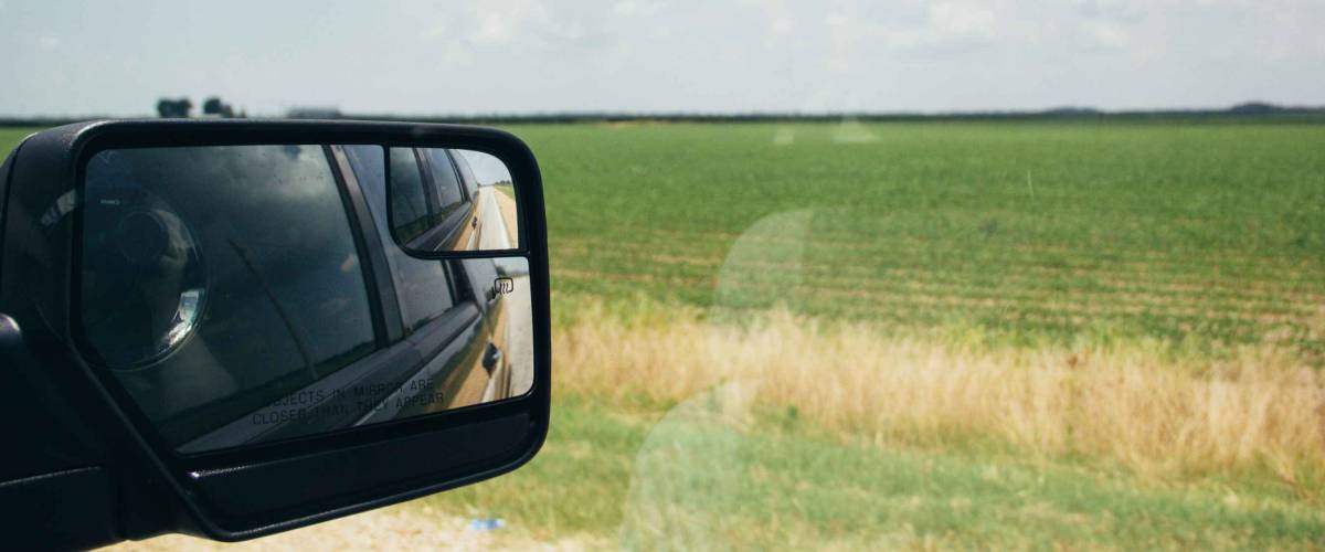 Driving down the highway on a road trip in the Southern United States. Picture of the car passenger side mirror and the farm fields off the side of the road. Mississippi State.