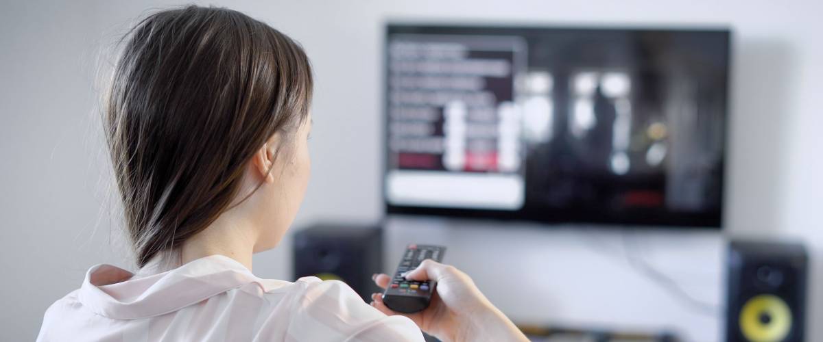 a young woman with dark hair is in her quarters, she sits in front of the TV and switches TV channels, a woman is seen watching a movie, a domesticer likes thrillers