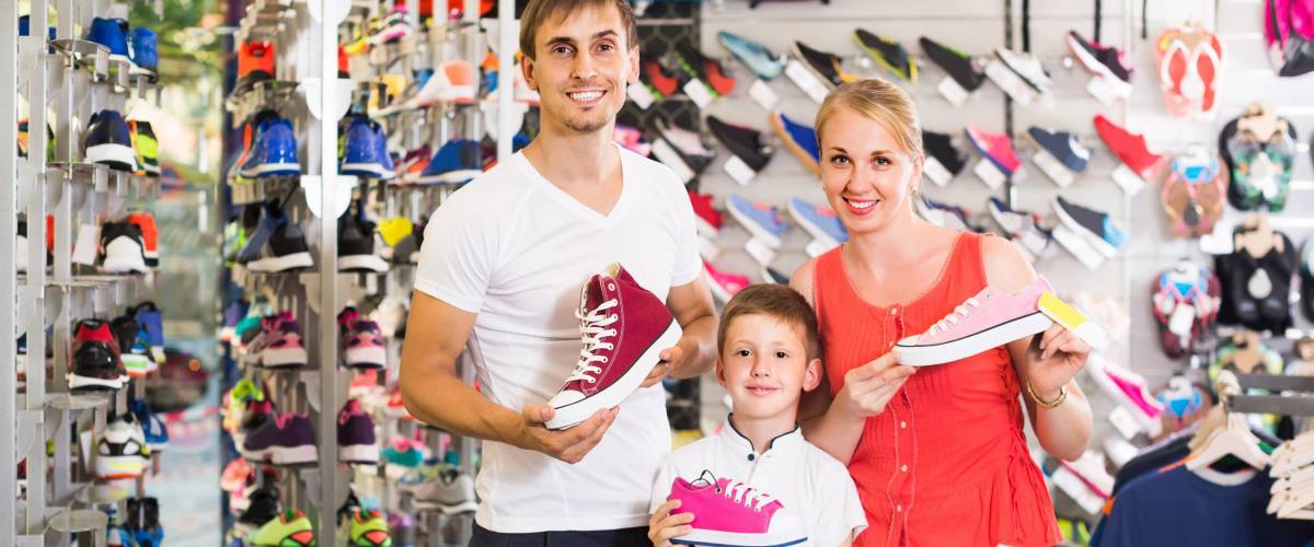 smiling spanish couple with boy choosing shoes in sport shop