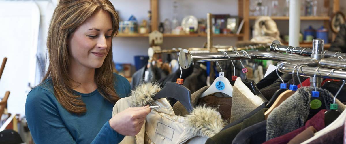 Female Shopper In Thrift Store Looking At Clothes