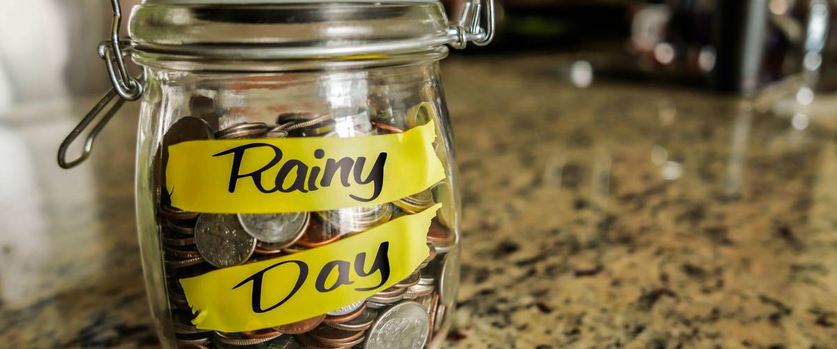Rainy Day Money Jar. A clear glass jar filed with coins and bills, saving money. The words