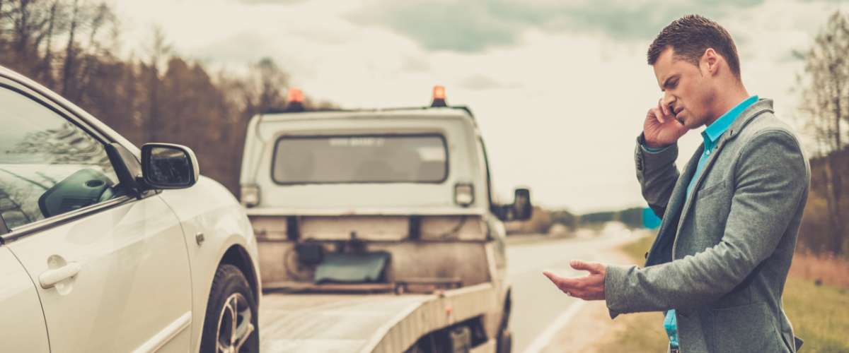 Man calling while tow truck picking up his broken car