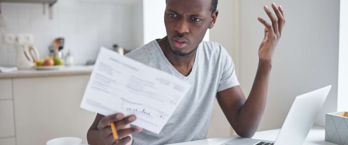 Indignant angry irritated male sitting at kitchen table, looking at papers in shock, astonished with amount of unpaid bills