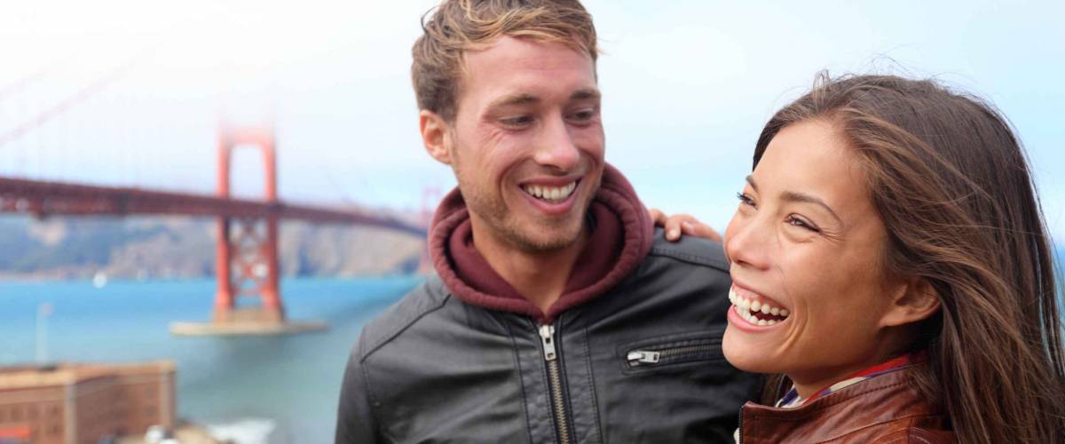 Happy young couple laughing in San Francisco by Golden Gate Bridge. Interracial young modern couple, Asian woman, Caucasian man.