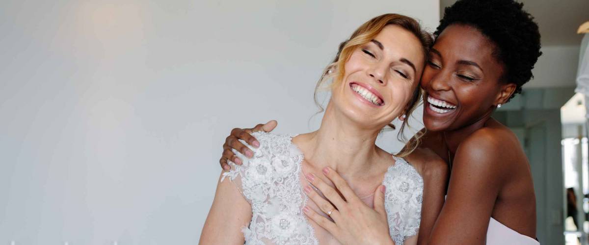 Gorgeous bride in wedding gown having fun with bridesmaid in hotel room.