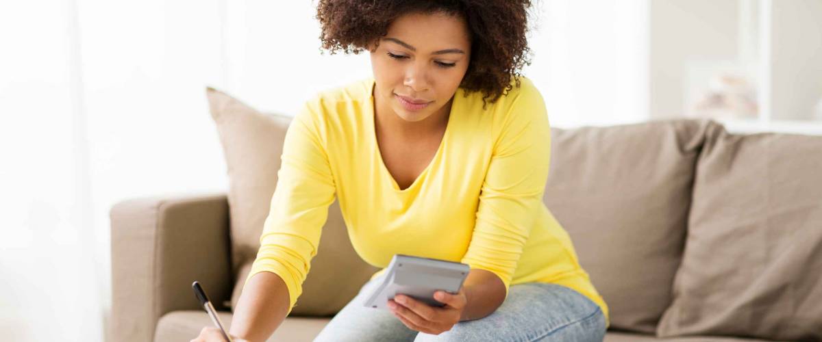 budget, finances and people concept - african american woman with papers and calculator counting money at home