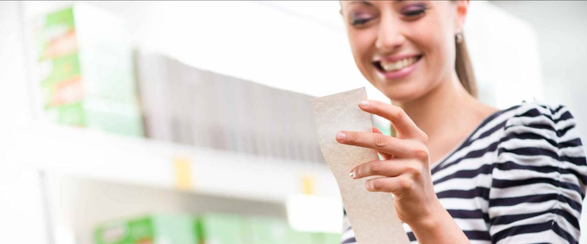 Smiling young woman holding a long grocery receipt at supermarket.