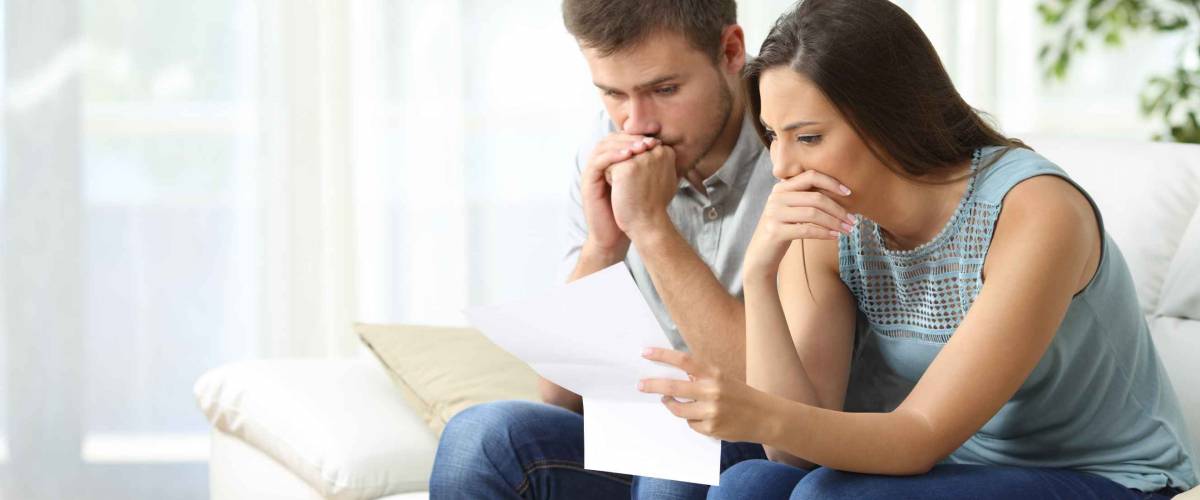 Worried couple reading an important notification in a letter sitting on a couch in the living room at home