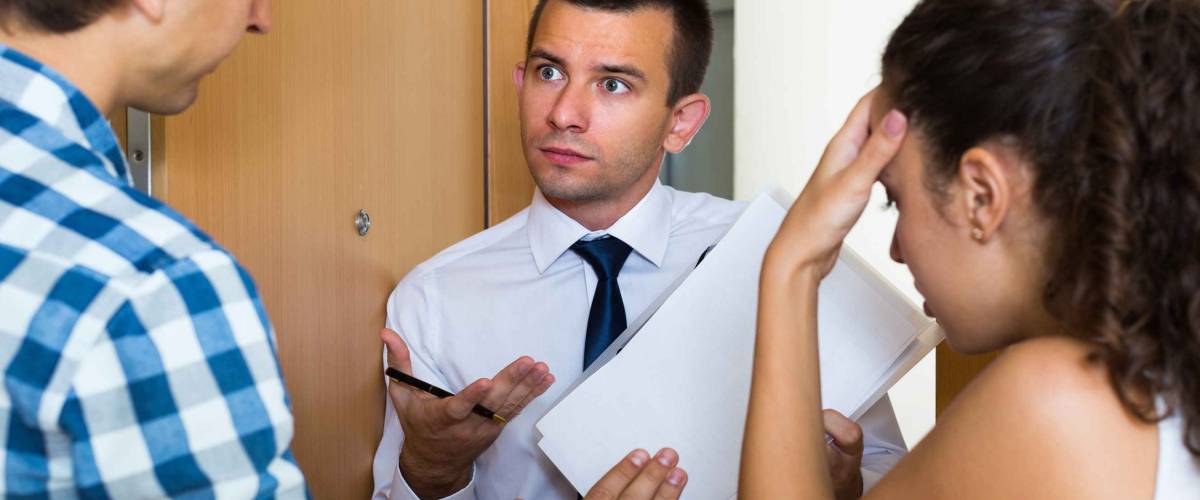Debt collector and sad young spouses with overdue payment at the doorway