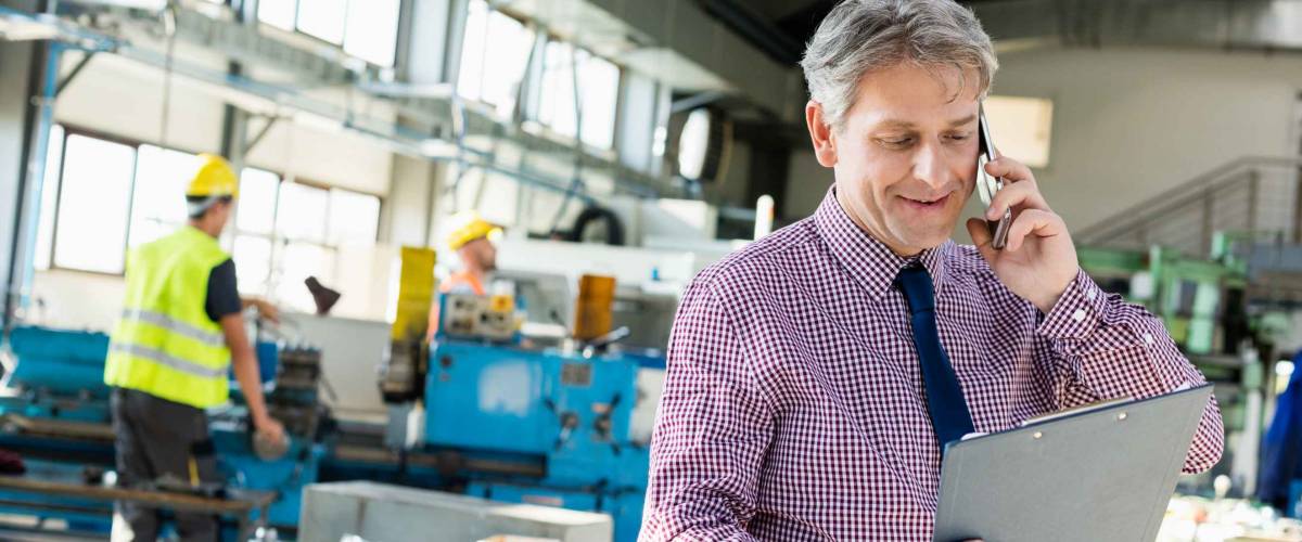 Man looks at clipboard while talking on mobile phone in industrial setting