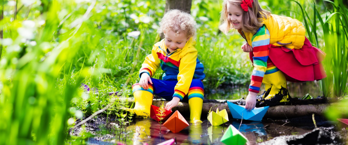 Children play with colorful paper boats in a small river on a sunny spring day.