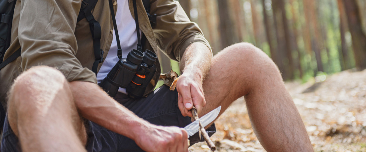 Young man whittling a stick in the woods