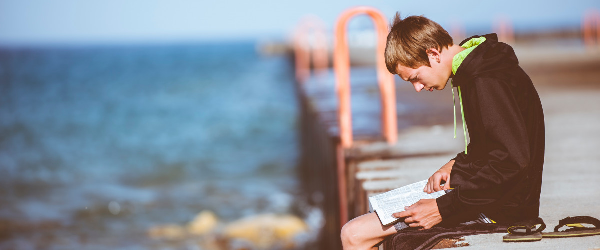 Young man reading on a dock pier looking out over the ocean calm